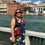 The author standing by a canal in Venice, Italy wearing a blue dress, red foldie, and her hamsa necklace