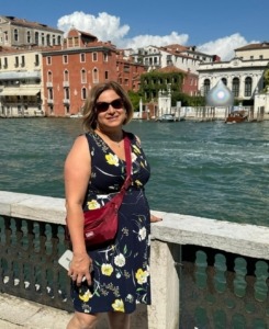 The author standing by a canal in Venice, Italy wearing a blue dress, red foldie, and her hamsa necklace